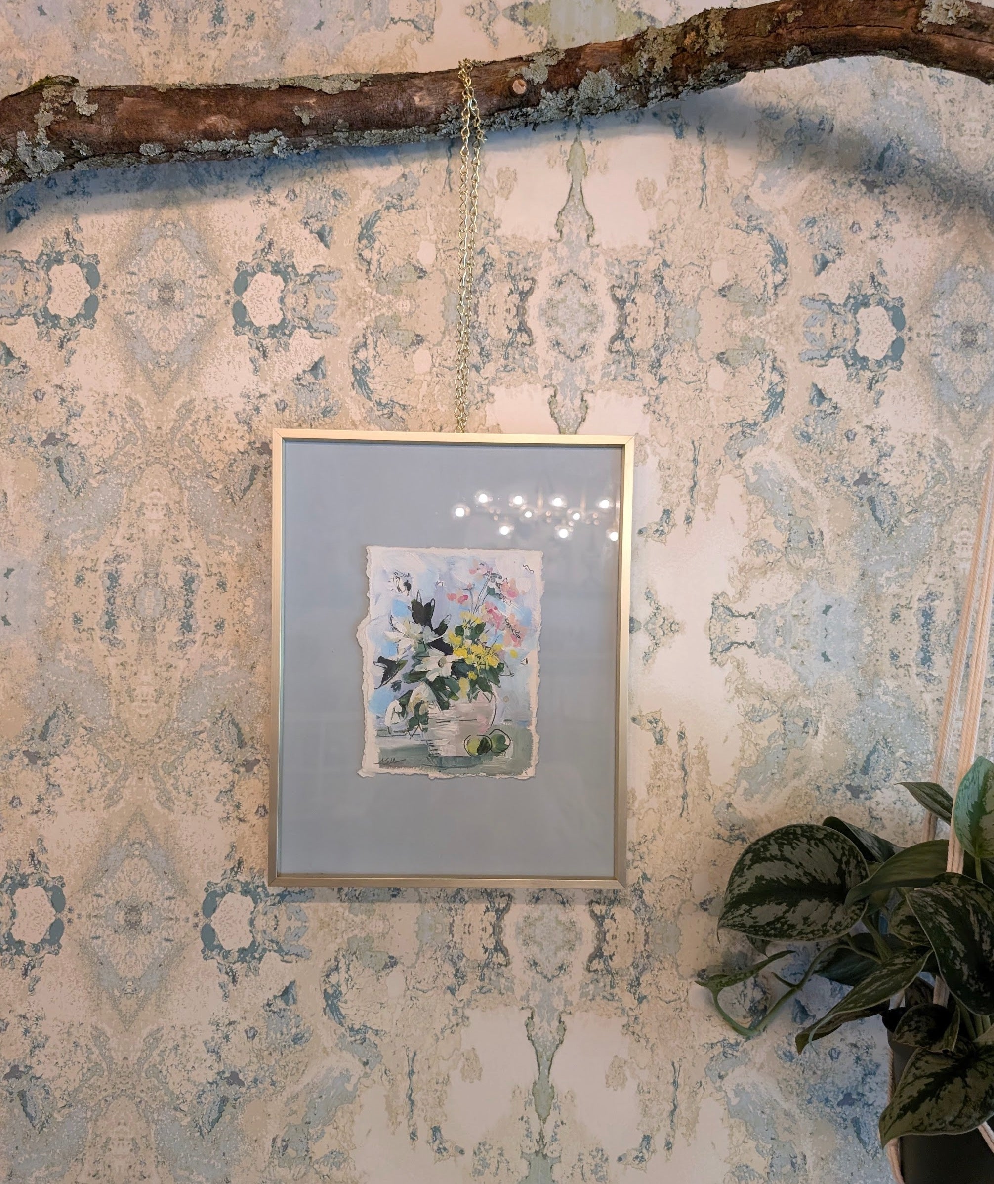 Framed artwork on a decorative wall with a branch and plant