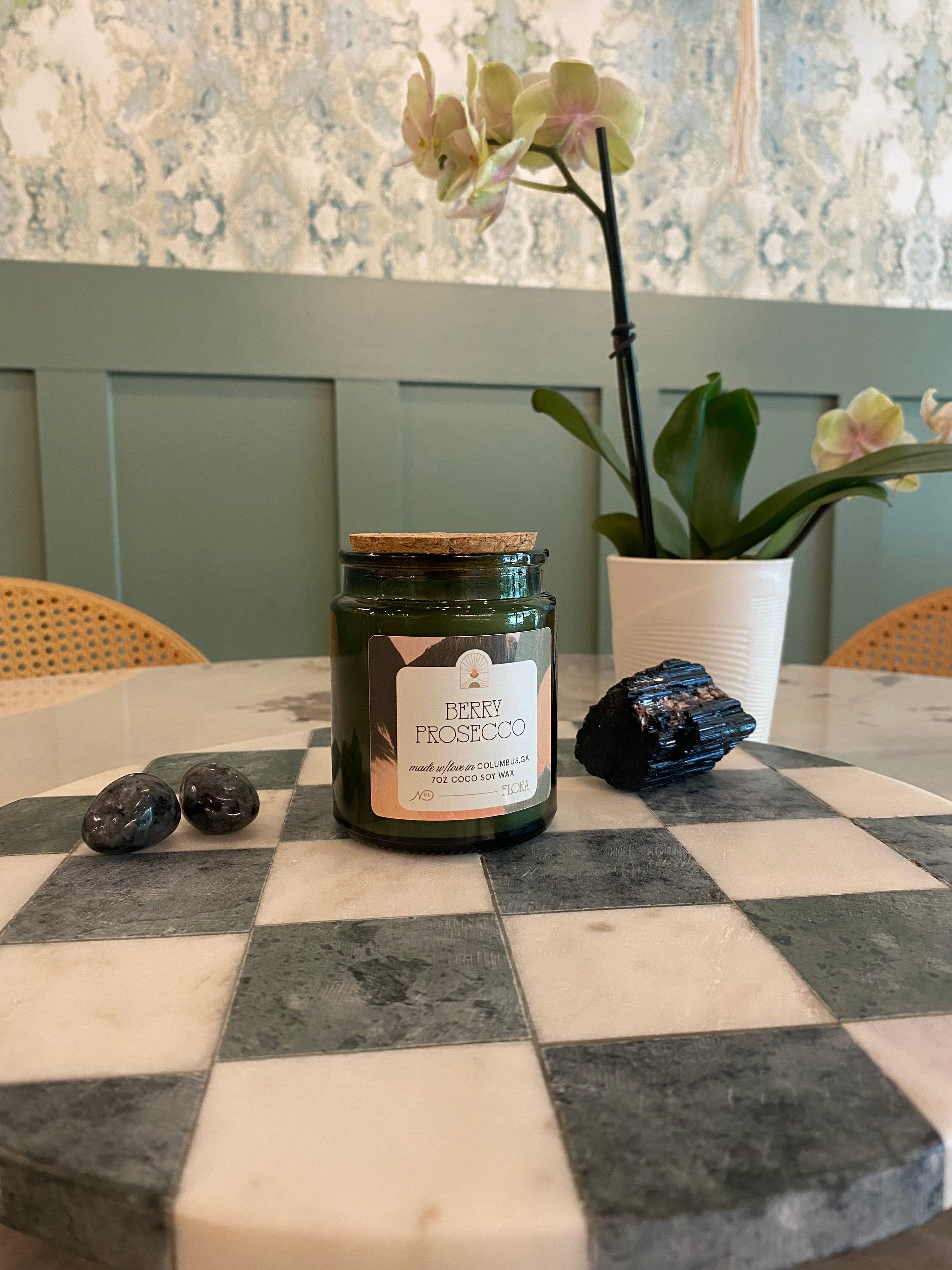 Jar of candle wax on a checkered table with flowers and decorative stones.