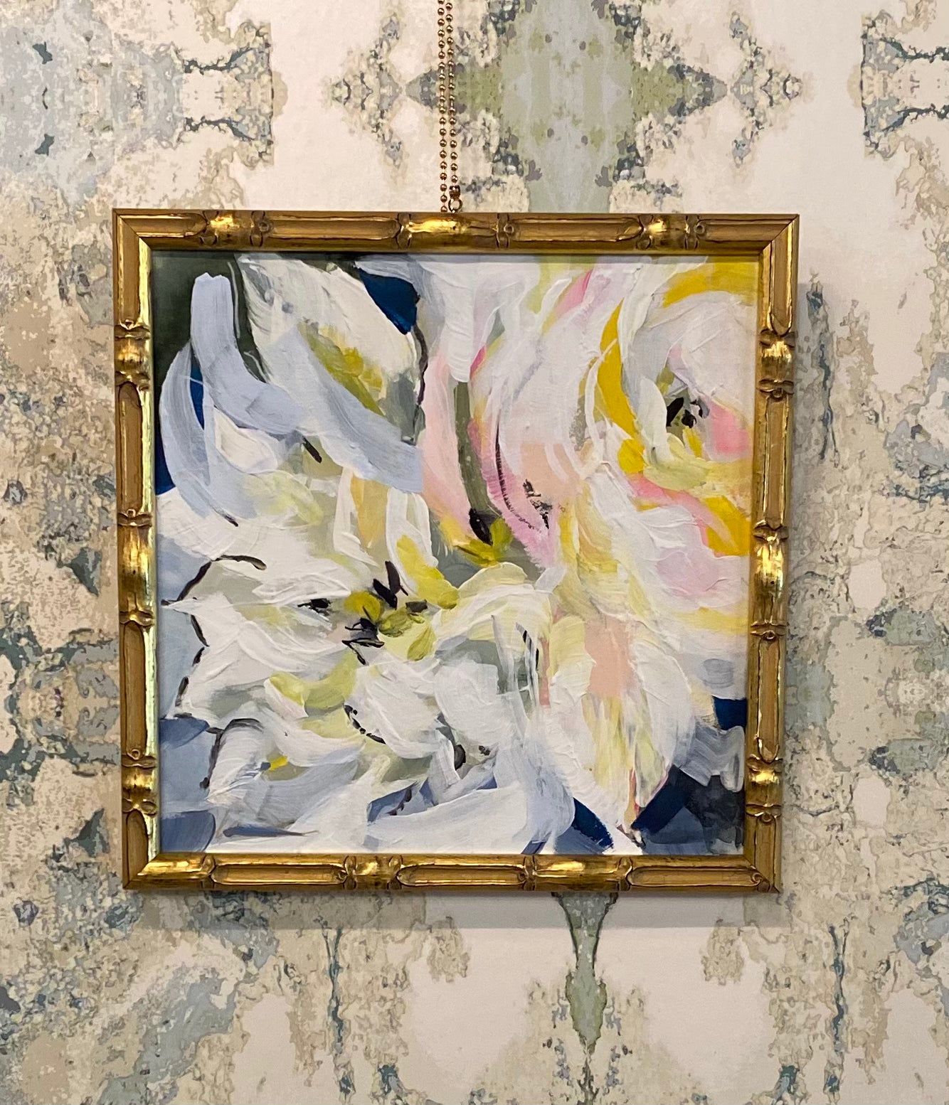 An abstract floral painting in a distressed gold frame, hanging on a heavily patterned wallpapered wall.