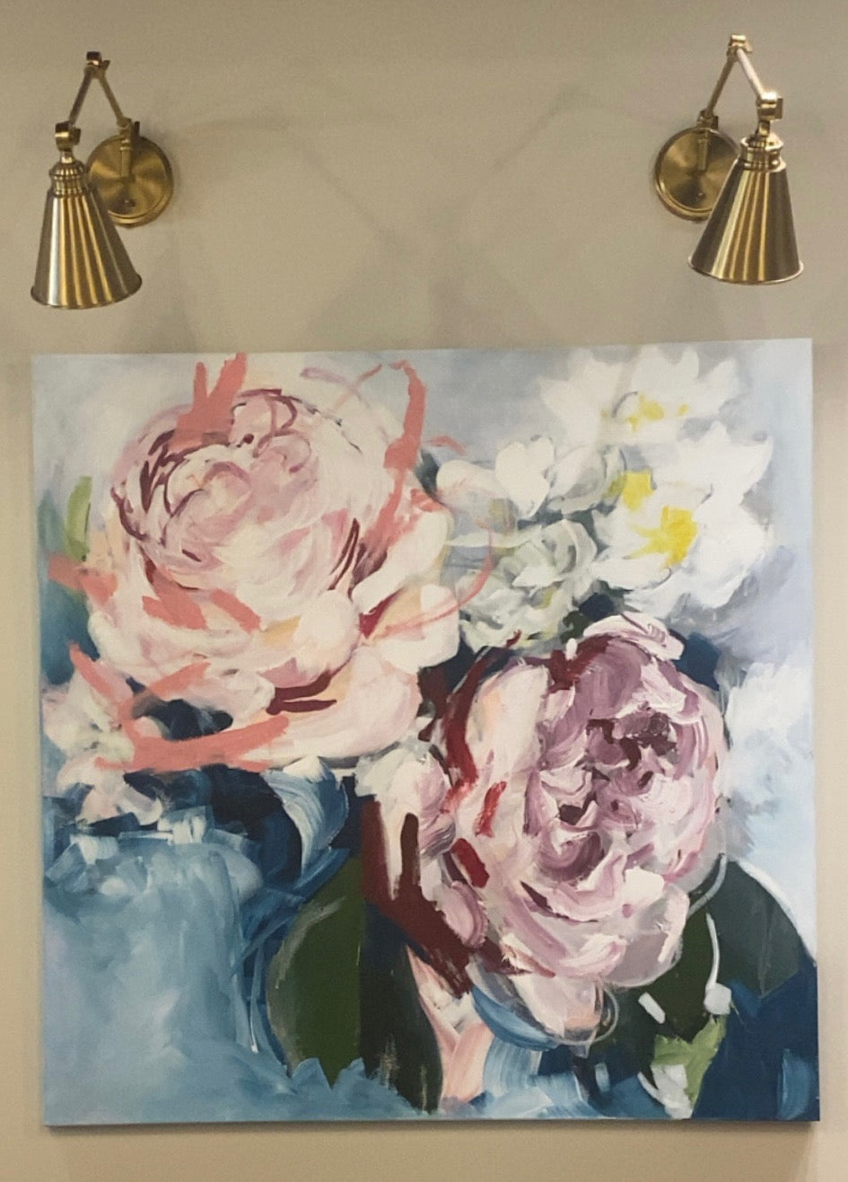 Floral painting on a wall with two gold sconces above.