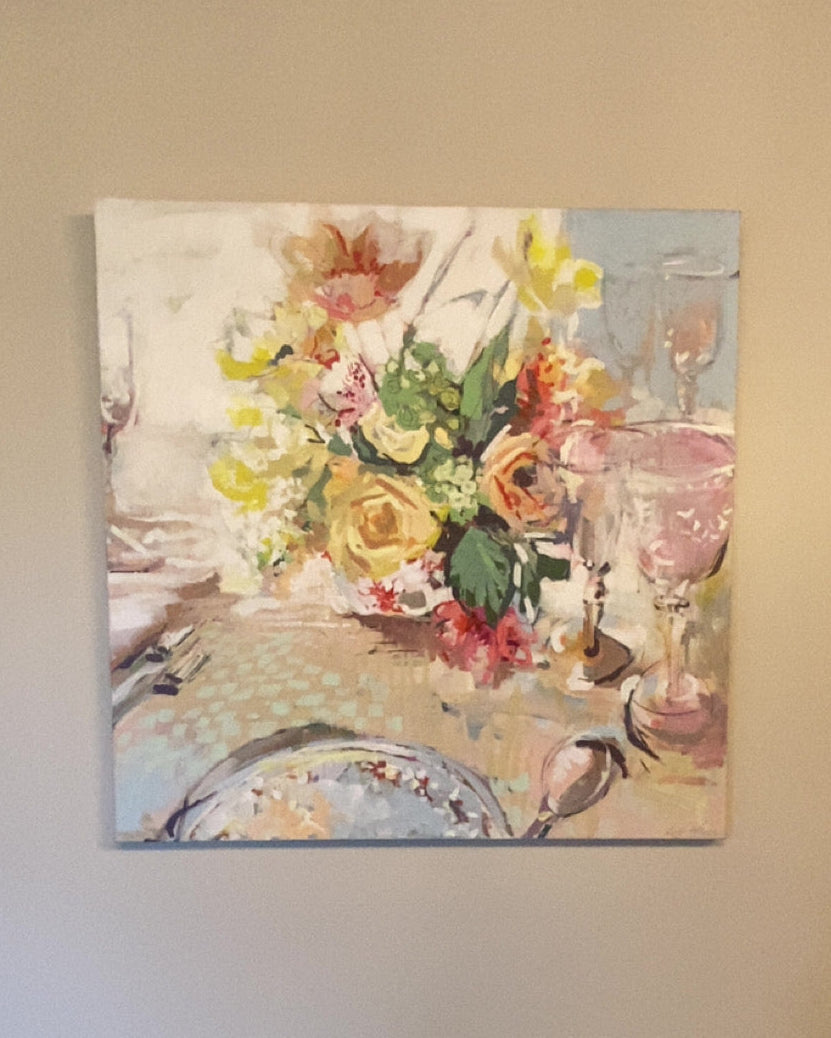 Painting of a floral table setting on a wall above a small table with decorative items.