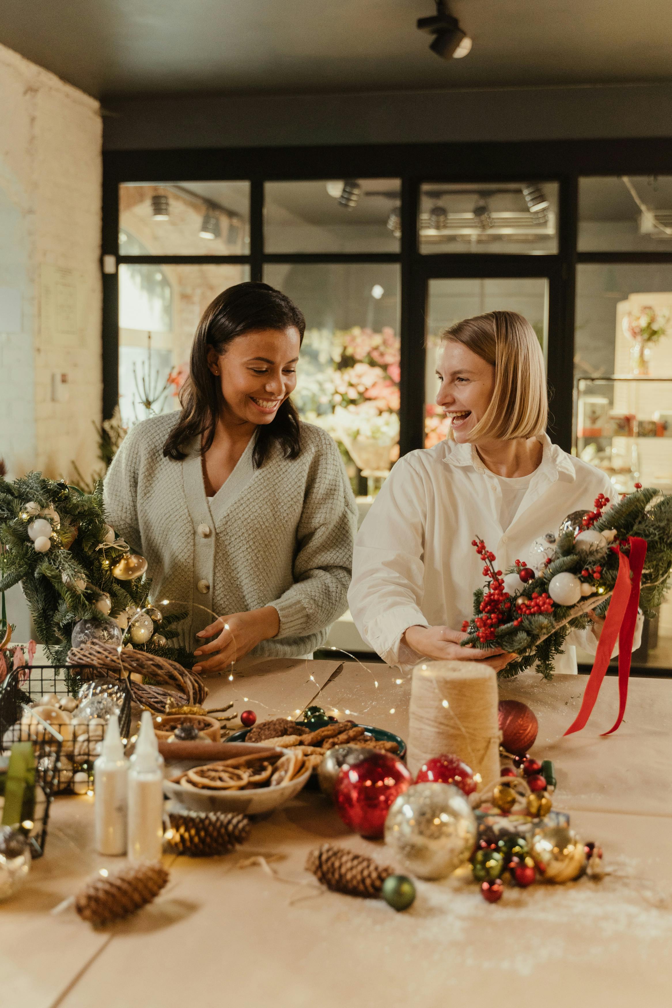Two women working on a table with Christmas decorations in a cozy indoor setting.